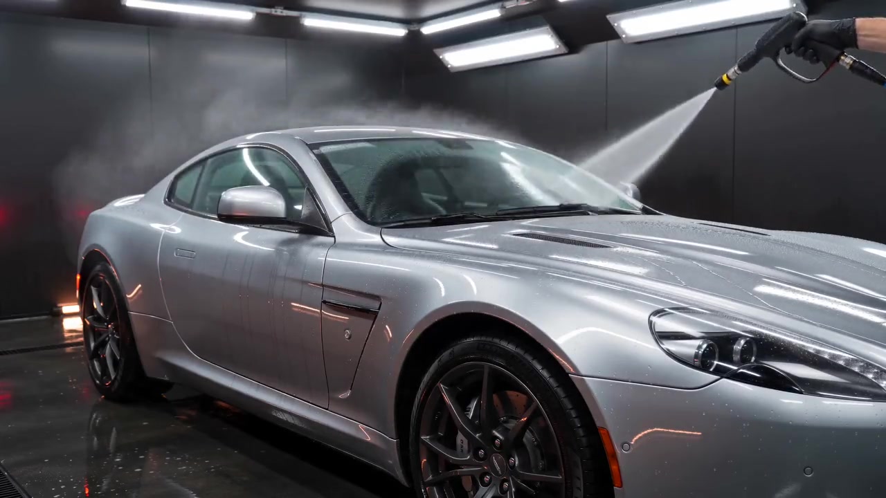 Silver grand touring coupe being rinsed in a charcoal detailing studio